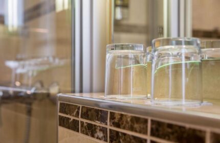 Bathroom detail in a gay-friendly Hotel Expo Frankfurt City Centre. Glasses on a tiled counter, reflecting the shower. Modern, clean design.