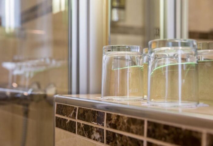 Bathroom detail in a gay-friendly Hotel Expo Frankfurt City Centre. Glasses on a tiled counter, reflecting the shower. Modern, clean design.