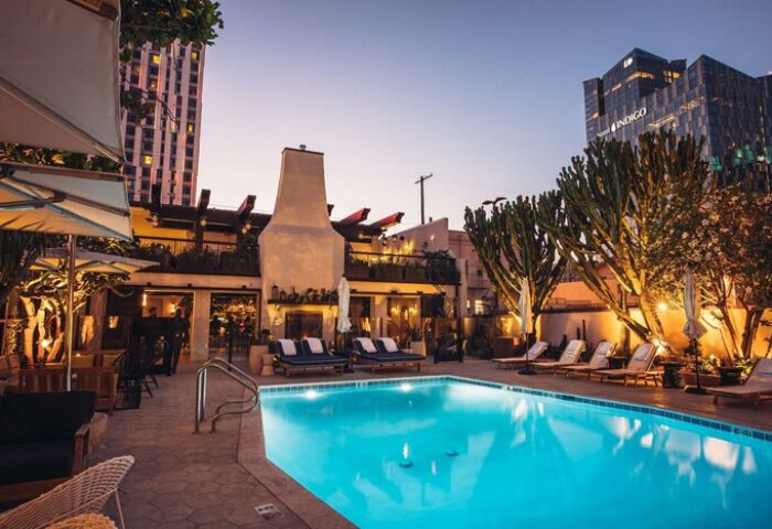 Hotel Figueroa, In The Unbound Collection By Hyatt, gay-friendly hotel. Poolside view at dusk, with lounge chairs and city buildings in the background.