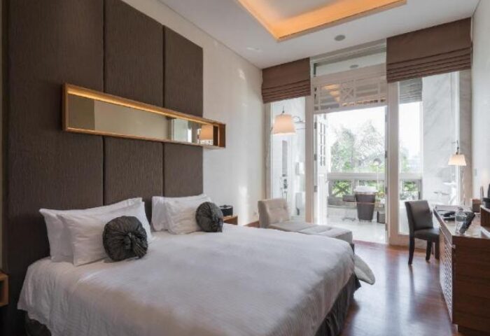 Hotel Fort Canning gay-friendly hotel room. King bed with white linens, brown headboard, and balcony. Upscale gay travel lodging.