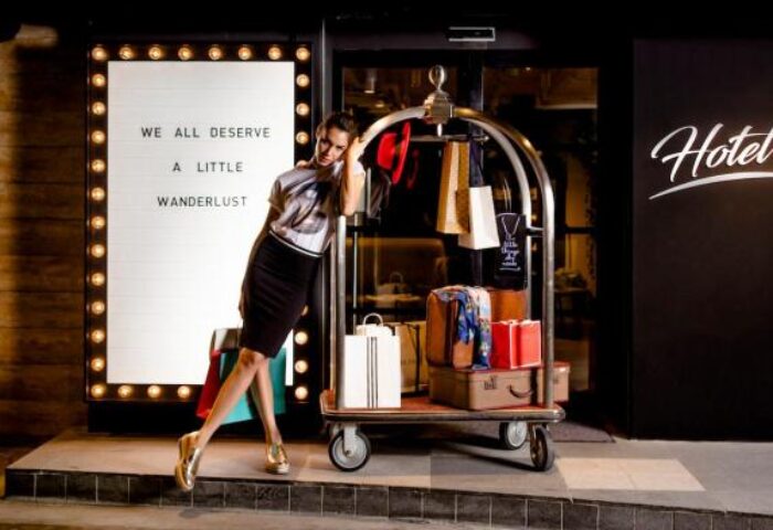 Hotel G Singapore: Woman poses with luggage cart in front of the gay-friendly hotel. Sign reads We all deserve a little wanderlust.