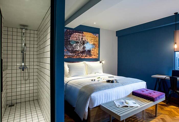 Hotel G Yangon gay-friendly hotel room. Features a shower, bed with art above, and bench. Modern design for gay travelers in Yangon.
