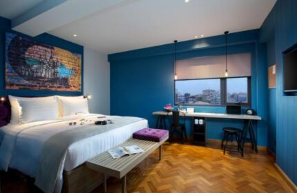 Hotel G Yangon gay-friendly hotel room. Queen bed with art, desk, and city view. Modern design, blue walls, and wooden floor. Comfortable stay.