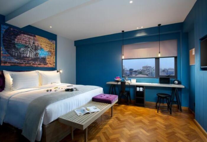 Hotel G Yangon gay-friendly hotel room. Queen bed with art, desk, and city view. Modern design, blue walls, and wooden floor. Comfortable stay.