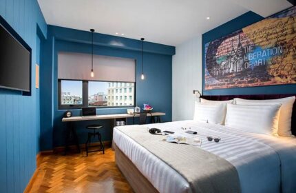 Hotel G Yangon's gay-friendly room. Blue walls, wooden floors, a bed with white linens, and a desk by the window. Art on the wall.