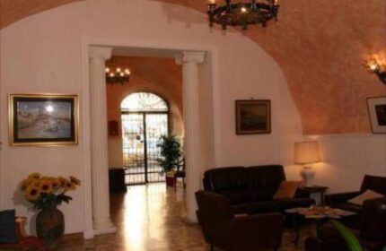 Hotel Giubileo's lobby, a gay-friendly hotel. Seating area with sofas, chairs, and artwork. Chandelier and arched doorway. Welcoming space.