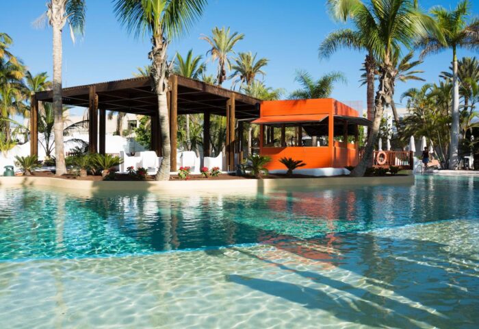 Hotel Gran Canaria Princess Adults Only pool view. Gay-friendly hotel with clear water, palm trees, orange bar and wooden structure.