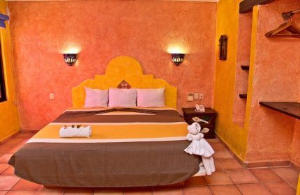Hotel Hacienda Maria Bonita gay-friendly room. Queen bed, vibrant orange and yellow walls, and a towel animal on the bed. Relaxing stay.