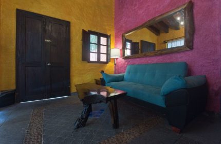 Hotel Hacienda Maria Bonita's gay-friendly room. A blue sofa sits beneath a rustic mirror. Yellow and pink walls add vibrant color.
