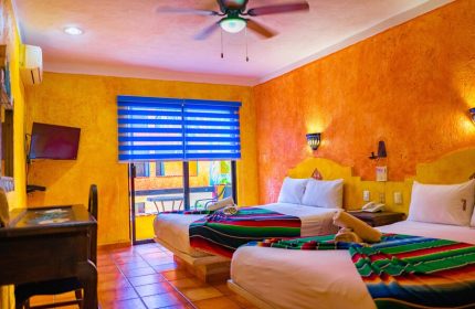 Gay-friendly Hotel Hacienda Maria Bonita room. Two beds with colorful blankets, bright walls, and a ceiling fan. Perfect for gay travel.