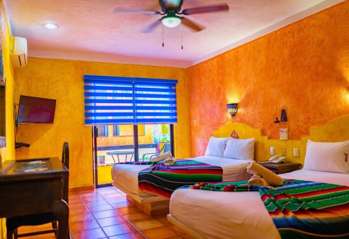Gay-friendly Hotel Hacienda Maria Bonita room. Two beds with colorful blankets, bright walls, and a ceiling fan. Perfect for gay travel.