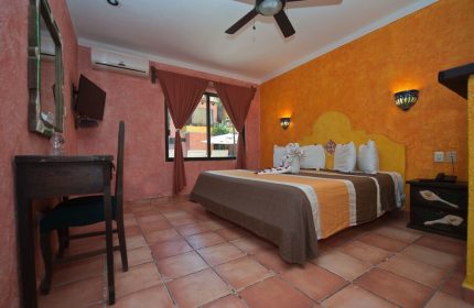 Hotel Hacienda Maria Bonita's gay-friendly room. Queen bed with swan towels, orange walls, and terracotta tile floor. Comfy stay for gay travelers.