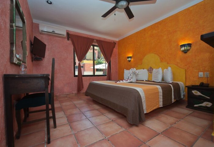 Hotel Hacienda Maria Bonita's gay-friendly room. Queen bed with swan towels, orange walls, and terracotta tile floor. Comfy stay for gay travelers.