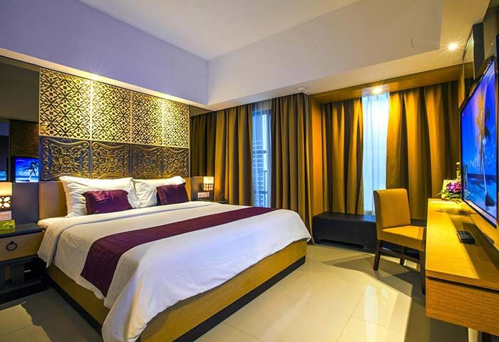Hotel Horison Seminyak Bali gay-friendly hotel room. Bed with purple accents, TV, chair, and decorative headboard. Luxury accommodations in Bali.