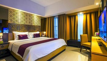 Hotel Horison Seminyak Bali gay-friendly hotel room. Bed with purple accents, TV, chair, and decorative headboard. Luxury accommodations in Bali.