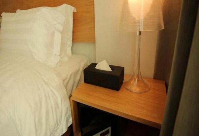 Hotel ITW gay-friendly hotel room: Bed with white linens, bedside table with lamp, tissue box, and safe. Comfortable stay for gay travelers.