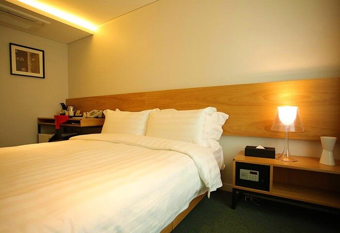 Hotel ITW gay-friendly room: queen bed with white linens, desk, and nightstand with lamp. A comfortable stay for gay travelers.