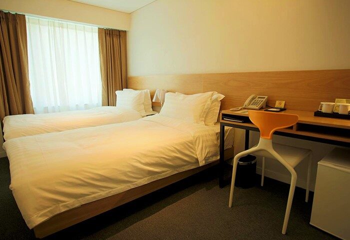Hotel ITW gay-friendly room with two beds, desk, and chair. Modern design, clean lines, and comfortable for travelers. Ideal for gay travel.