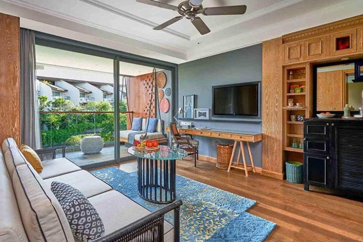 Hotel Indigo Bali Seminyak Beach suite. Living area with sofa, desk, TV, balcony. Gay-friendly hotel, stylish interior design.