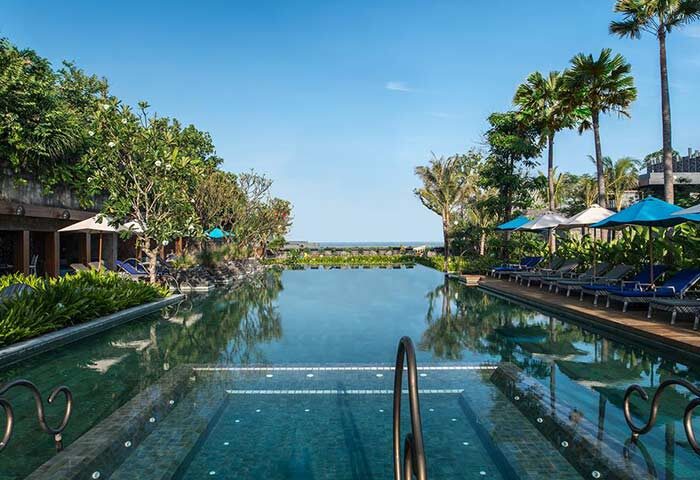Hotel Indigo Bali Seminyak Beach pool view. Gay-friendly hotel with palm trees, lounge chairs, and ocean view. Ideal for gay travel.
