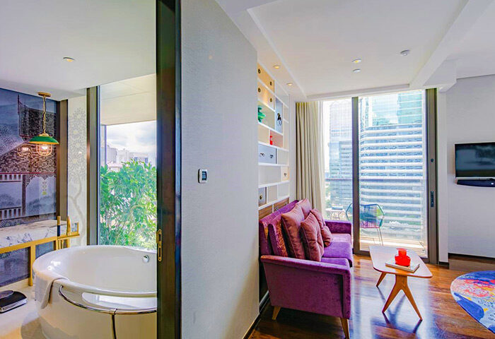 Hotel Indigo Bangkok Wireless Road gay-friendly room. Bathtub view, purple sofa, and Bangkok skyline. Luxury travel at its finest.