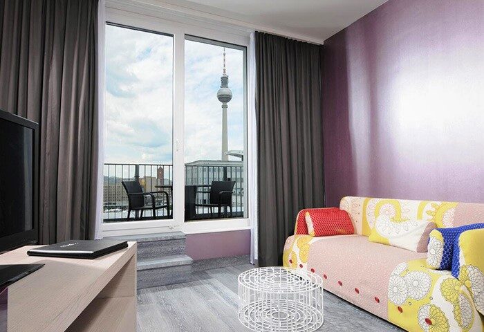 Hotel Indigo Berlin-Alexanderplatz room with TV tower view. Gay-friendly hotel with balcony, seating, and colorful decor. Berlin travel.