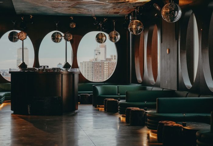 Bar at Hotel Indigo Lower East Side, a gay-friendly hotel. Disco balls hang above green sofas and oval windows with city views.