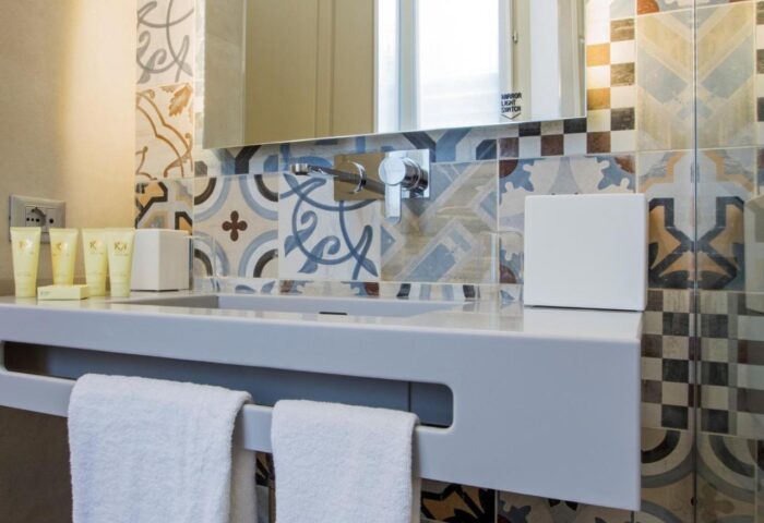 Hotel Indigo Milan Corso Monforte gay-friendly hotel bathroom. Sink with toiletries, colorful tiles, and white towels. Modern design.