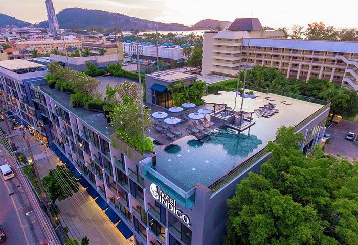 Hotel Indigo Phuket Patong, a gay-friendly hotel. Rooftop pool, lounge chairs, umbrellas, and greenery. City and ocean views. Ideal for gay travel.