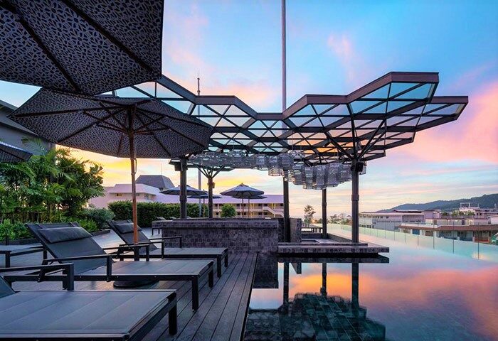 Hotel Indigo Phuket Patong gay-friendly hotel rooftop pool at sunset. Modern design, lounge chairs, umbrellas, and scenic views.