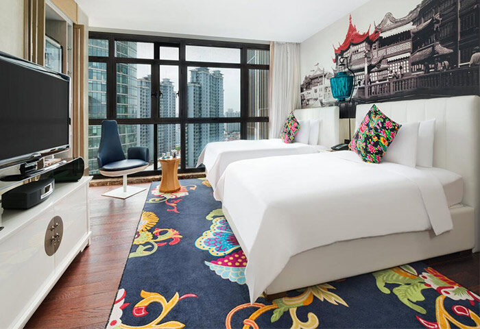 Hotel Indigo Shanghai On The Bund gay-friendly hotel room. Two beds, city view, colorful rug, and Shanghai-themed wall art. Modern design.