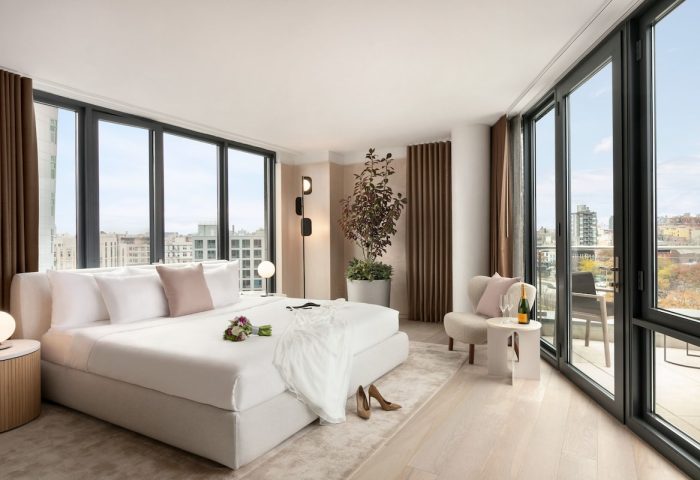 Hotel Indigo Williamsburg Brooklyn gay-friendly hotel room. King bed, floor-to-ceiling windows, city view. Champagne, shoes, and dress on the bed.