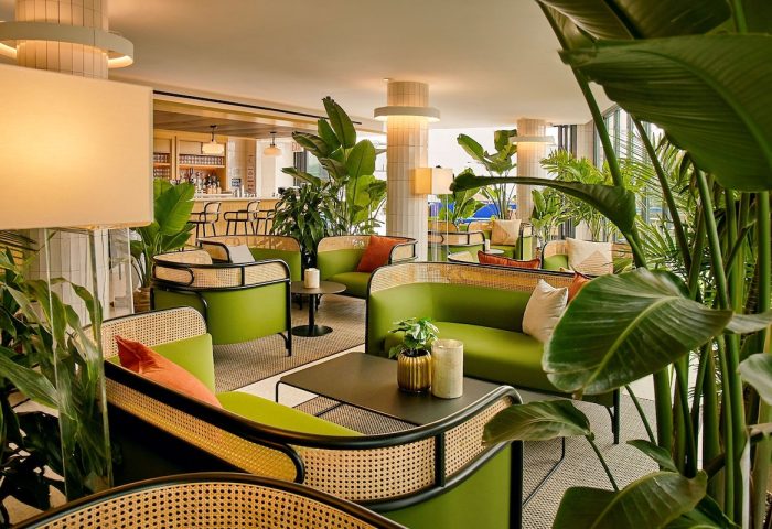Hotel Indigo Williamsburg, Brooklyn. Gay-friendly hotel lounge area with green sofas, rattan details, plants, and a bar in the background.