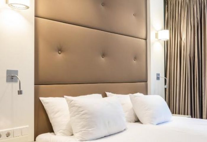Hotel JL No76 gay-friendly hotel room. Queen bed with brown headboard, white pillows, and bedside table. Modern lamps and curtains.