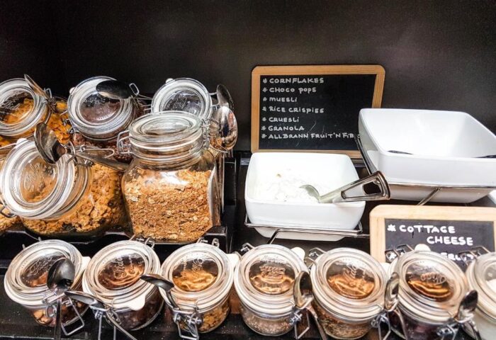 Breakfast buffet at gay-friendly Hotel JL No76: cereal, granola, muesli, cottage cheese, and other toppings in glass jars with serving spoons.