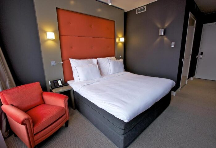 Hotel JL No76 gay-friendly room. Modern design, orange headboard, white linens, and a cozy red armchair. Ideal for gay travel in Amsterdam.