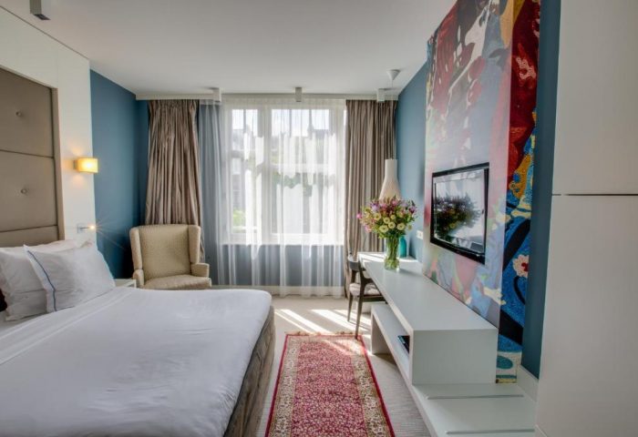 Hotel JL No76 gay-friendly room. Bedroom with bed, chair, TV, and desk. Modern design, colorful art. Gay travel in Amsterdam.