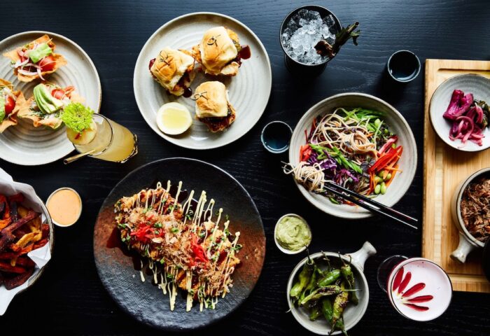 Hotel Kabuki, part of Jdv by Hyatt, gay-friendly hotel food. Dishes include sliders, noodles, fries, and cocktails on a dark table.