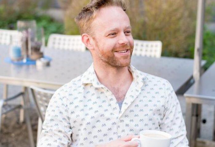 Gay man at Hotel Ku'Damm 101, a gay-friendly hotel. Man with coffee outdoors, smiling. Travel advice for gay men in Berlin.