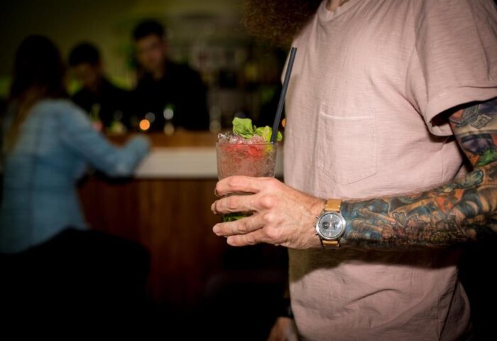 Man with tattoos holding a cocktail at Hotel Ku'Damm 101 bar. Gay-friendly hotel in Berlin, Germany. Nightlife, drinks.