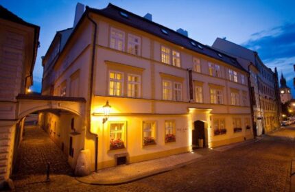 Hotel Leonardo Prague exterior at dusk. Gay-friendly, pet-friendly hotel with illuminated windows and cobblestone street. Prague travel.