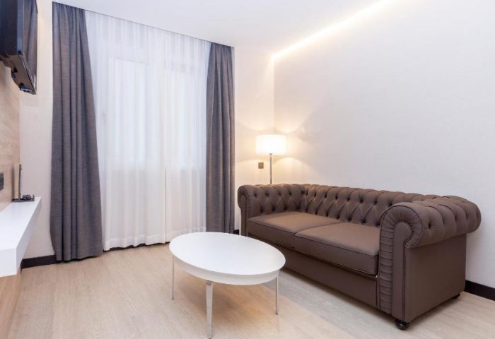 Hotel Liabeny room. Gay-friendly hotel room with brown leather sofa, white table, TV, curtains. Modern interior, comfortable for gay travelers.