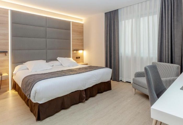 Hotel Liabeny's gay-friendly room. Modern design with a large bed, gray headboard, desk, and chair. Comfortable stay for gay travelers in Madrid.