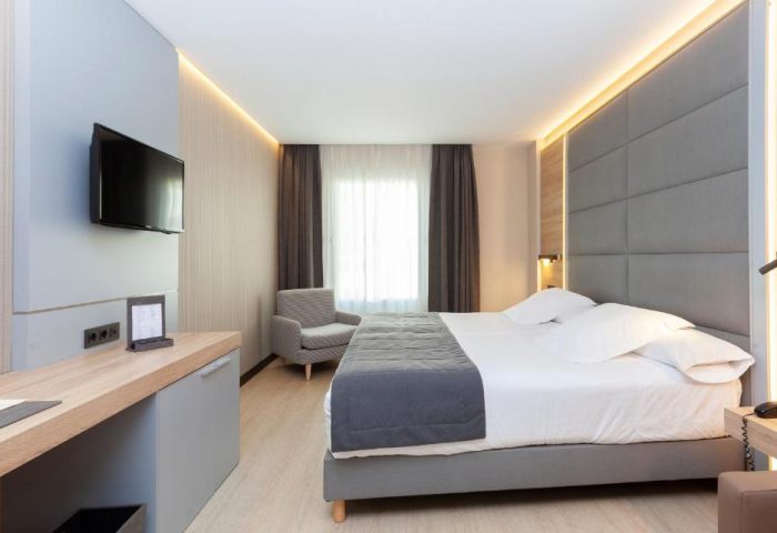Hotel Liabeny's gay-friendly room. Modern design, double bed with gray headboard, desk, TV, and armchair. Ideal for gay travel in Madrid.