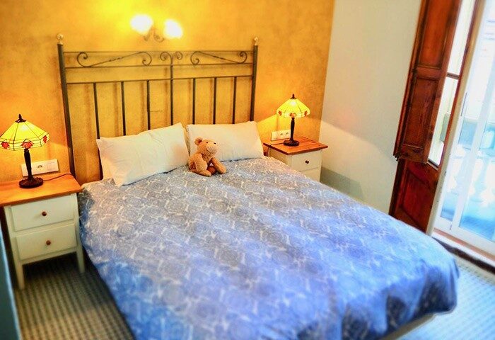 Bedroom at Hotel Liberty Sitges, a gay-friendly hotel. Double bed with a teddy bear, bedside tables with lamps, and an open door.