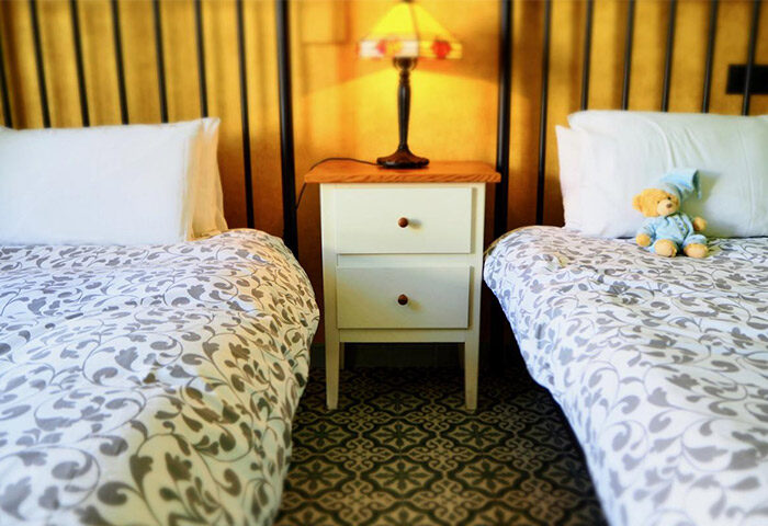 Hotel Liberty Sitges gay-friendly room. Twin beds, floral bedding, teddy bear, bedside table, lamp. Comfortable stay in Sitges, Spain.