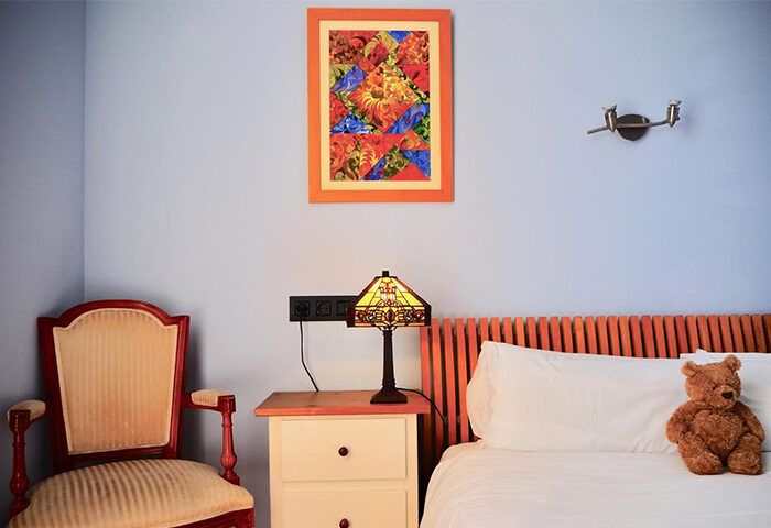 Gay-Friendly Hotel Liberty Sitges room. Cozy interior with bed, teddy bear, chair, lamp, and colorful artwork. Gay travel in Sitges, Spain.