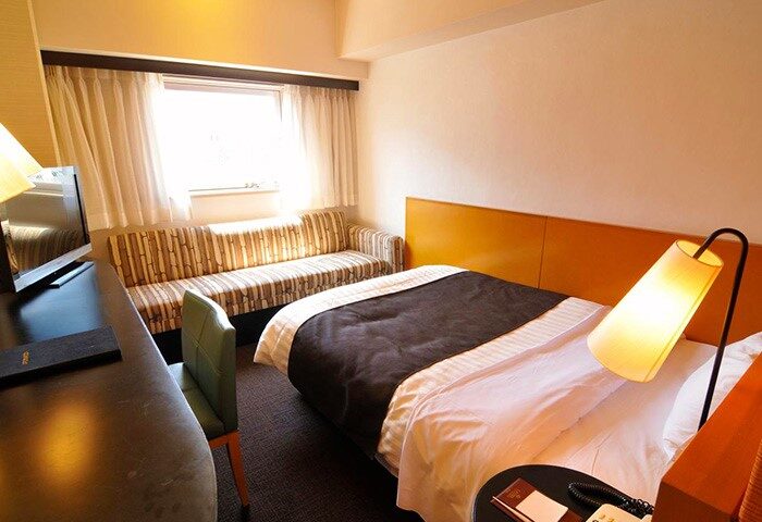 Hotel Listel Shinjuku's gay-friendly room. A bed with a brown duvet, a striped sofa, desk, chair, and bedside lamp. Comfortable stay in Tokyo.