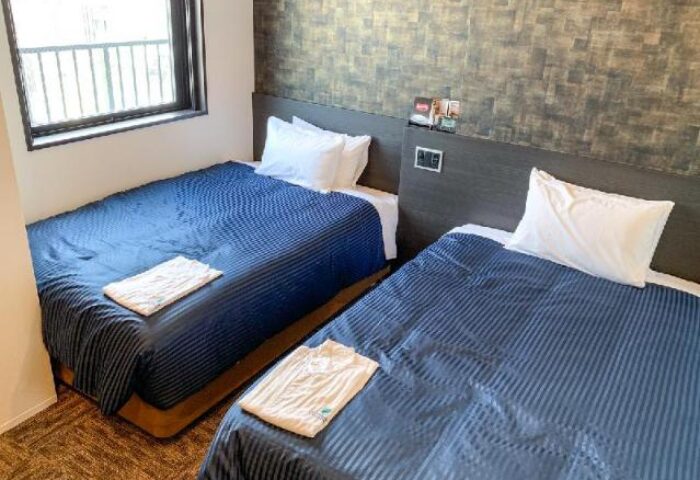 Hotel Livemax Shinjuku-Kabukicho room. Two twin beds with blue striped covers in a gay-friendly hotel. Clean, modern design. Window view.