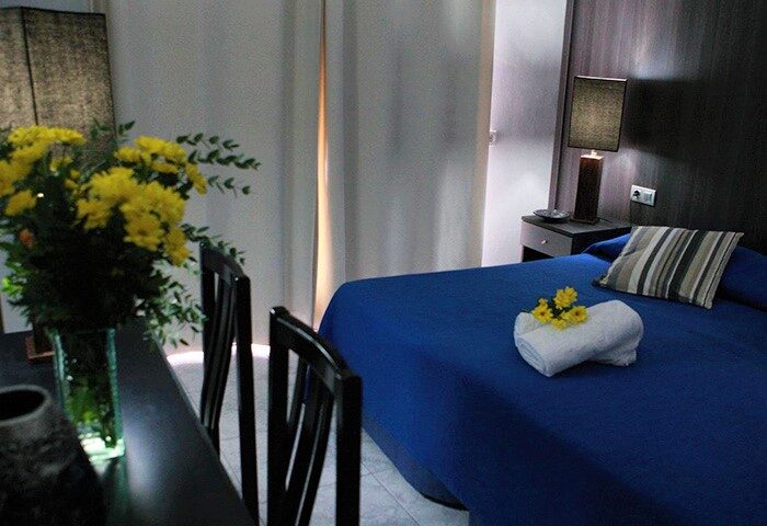 Hotel Los Globos gay-friendly hotel room. Blue bed with yellow flowers, striped pillow, and bedside table with lamp. Gay travel lodging.